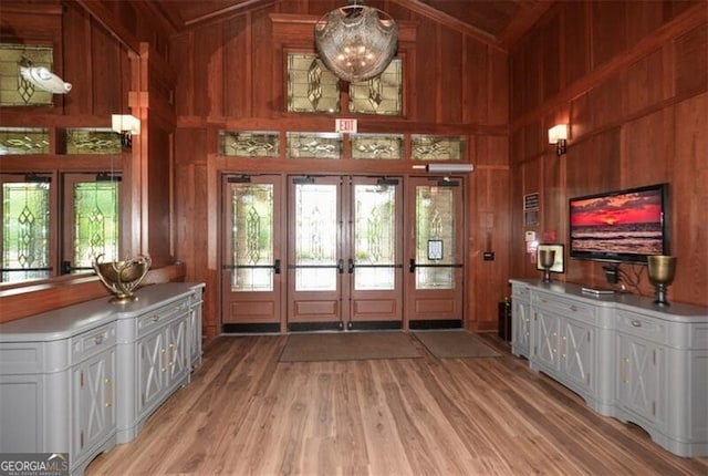 interior space featuring light wood finished floors, an inviting chandelier, french doors, wood walls, and high vaulted ceiling