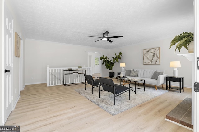 living area featuring baseboards, a textured ceiling, a ceiling fan, and wood finished floors