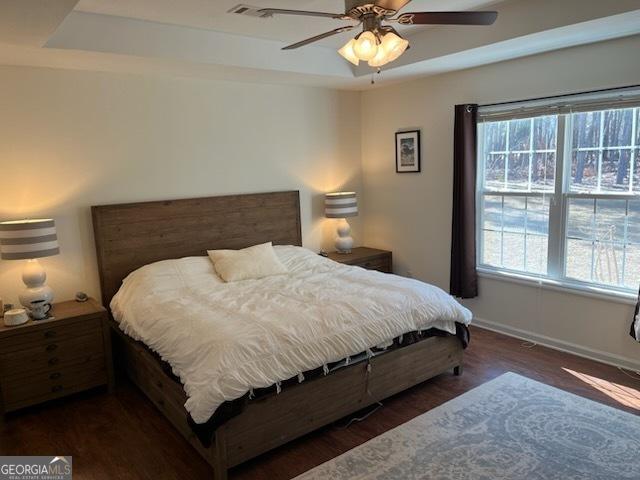 bedroom featuring a raised ceiling, ceiling fan, baseboards, and wood finished floors