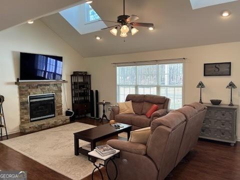 living room with a skylight, wood finished floors, and a stone fireplace