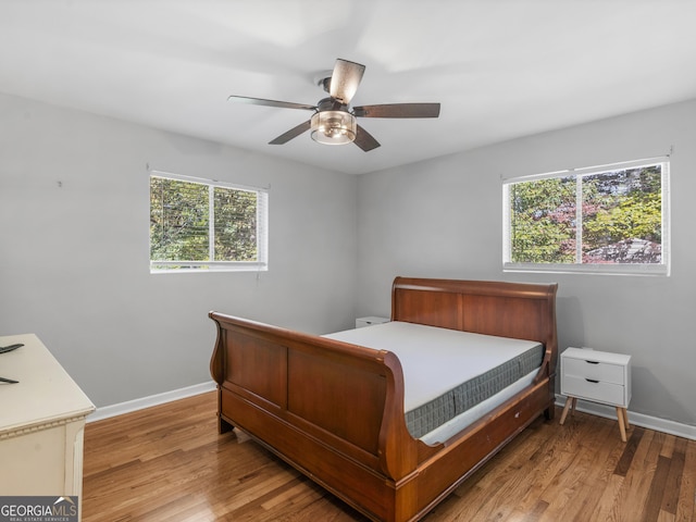 bedroom with ceiling fan, light wood finished floors, multiple windows, and baseboards