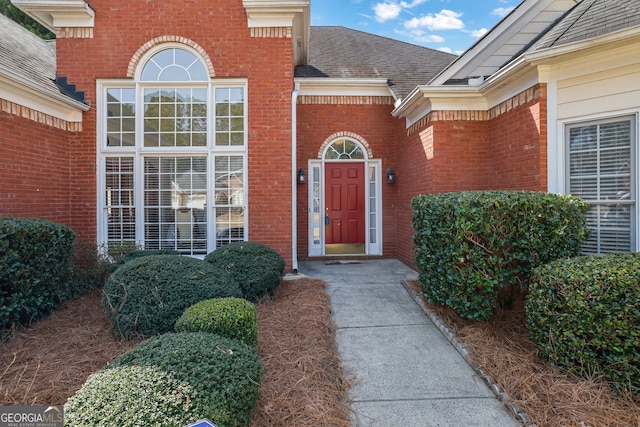 property entrance with roof with shingles and brick siding