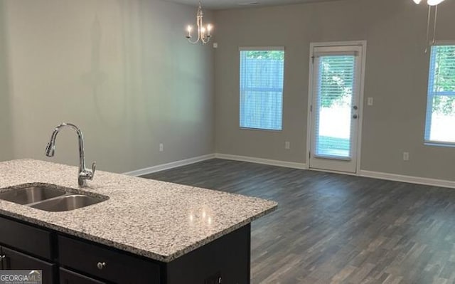 kitchen with dark wood-style flooring, a sink, light stone countertops, and baseboards