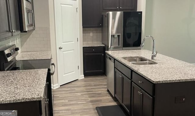 kitchen with a center island with sink, appliances with stainless steel finishes, wood finished floors, a sink, and backsplash