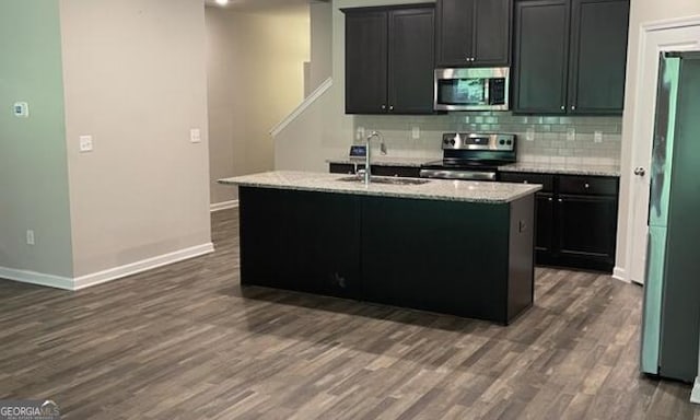 kitchen with stainless steel appliances, a sink, tasteful backsplash, dark wood finished floors, and a center island with sink