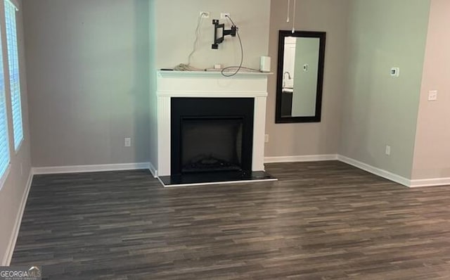 unfurnished living room featuring a fireplace with raised hearth, wood finished floors, and baseboards