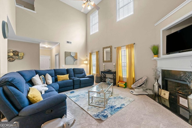 living area with carpet floors, crown molding, visible vents, a ceiling fan, and a high end fireplace