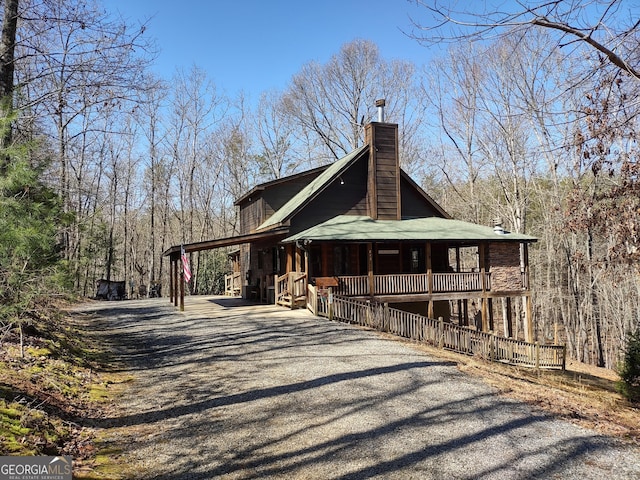 view of side of property featuring driveway, covered porch, and a chimney