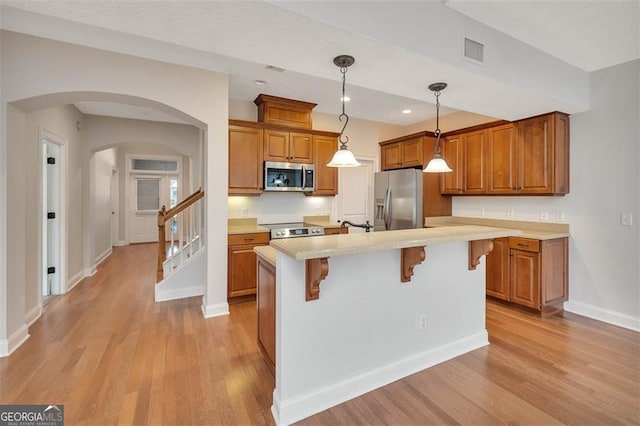 kitchen featuring visible vents, arched walkways, appliances with stainless steel finishes, brown cabinets, and light countertops