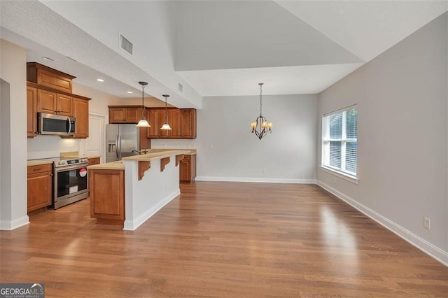 kitchen with stainless steel appliances, visible vents, an inviting chandelier, brown cabinetry, and a kitchen breakfast bar