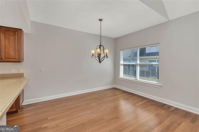 unfurnished dining area with light wood-type flooring, baseboards, and an inviting chandelier