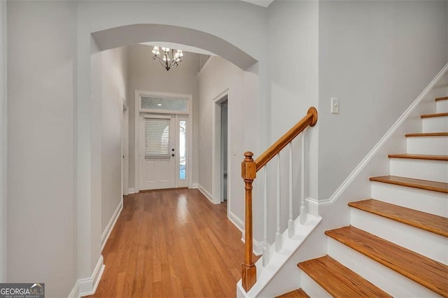 entrance foyer with light wood-style floors, arched walkways, baseboards, and stairs