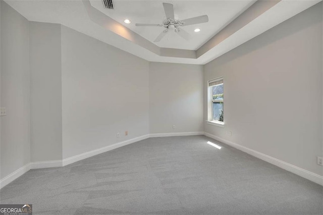 empty room with a tray ceiling, visible vents, and baseboards