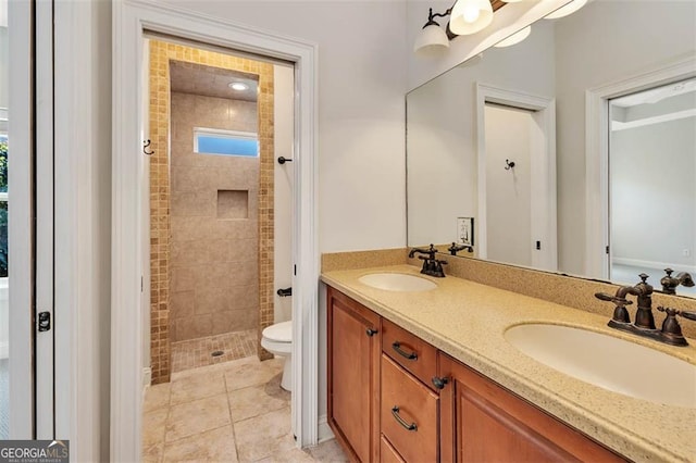 bathroom featuring tile patterned flooring, toilet, a sink, tiled shower, and double vanity