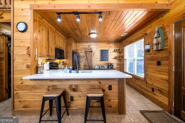 kitchen with a peninsula, wood walls, wood ceiling, light countertops, and black appliances