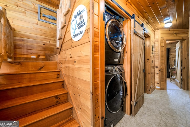 laundry area with wood ceiling, a barn door, wooden walls, and stacked washer / drying machine