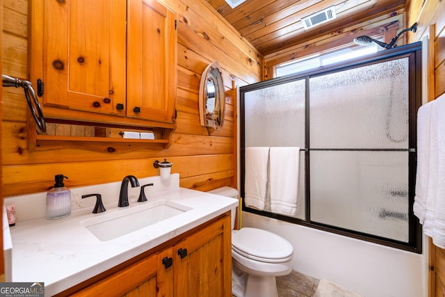 full bathroom featuring visible vents, toilet, shower / bath combination with glass door, vanity, and wood walls