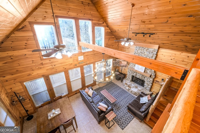 unfurnished living room with a fireplace, a ceiling fan, wood ceiling, wood walls, and high vaulted ceiling