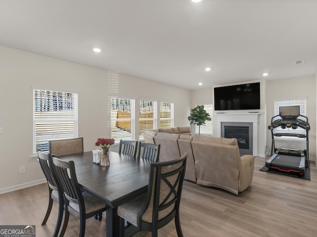 dining space featuring a glass covered fireplace, light wood-style flooring, baseboards, and recessed lighting