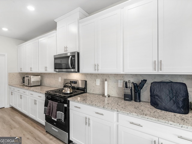 kitchen featuring stainless steel microwave, gas stove, backsplash, and white cabinetry