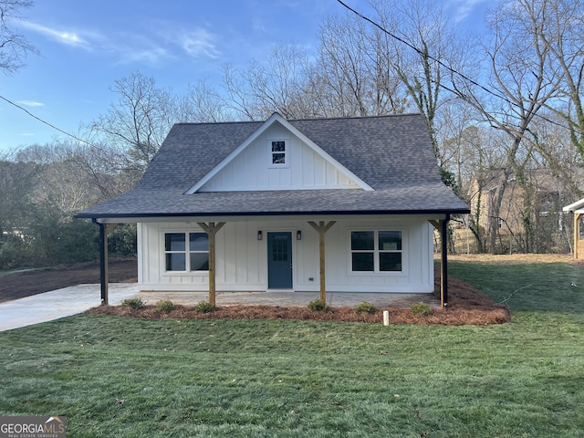 view of front of home featuring a shingled roof, a front yard, covered porch, and board and batten siding