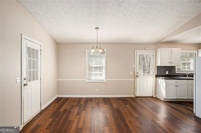 unfurnished dining area with baseboards, a textured ceiling, dark wood finished floors, and an inviting chandelier