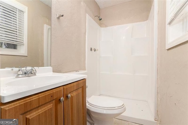 full bath featuring a textured wall, vanity, toilet, and walk in shower