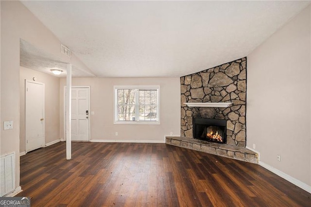 unfurnished living room with baseboards, visible vents, wood finished floors, and a stone fireplace