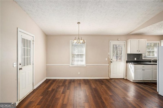 unfurnished dining area with a textured ceiling, baseboards, dark wood finished floors, and a notable chandelier