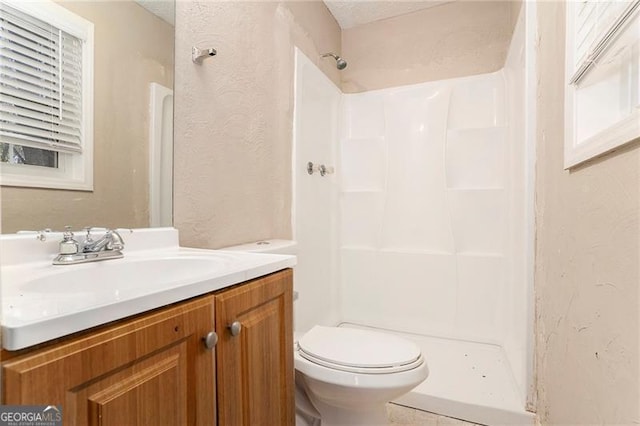 bathroom featuring a textured wall, vanity, toilet, and walk in shower