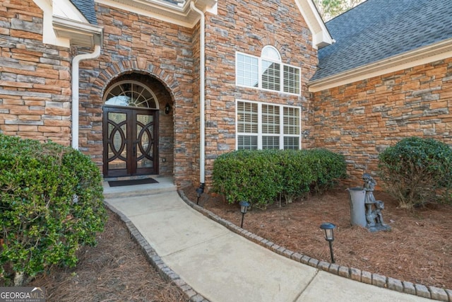 doorway to property with stone siding and a shingled roof