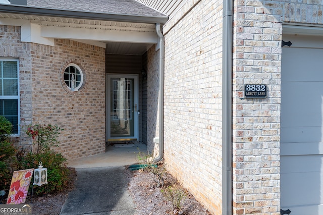 entrance to property featuring brick siding, a garage, and roof with shingles