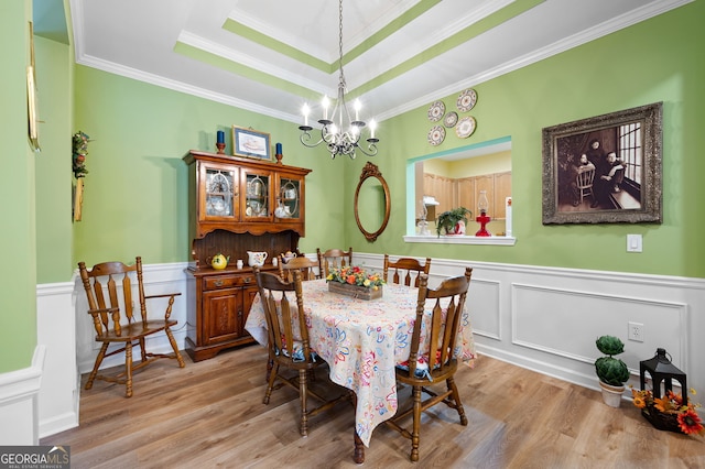 dining space featuring wood finished floors, an inviting chandelier, wainscoting, crown molding, and a raised ceiling