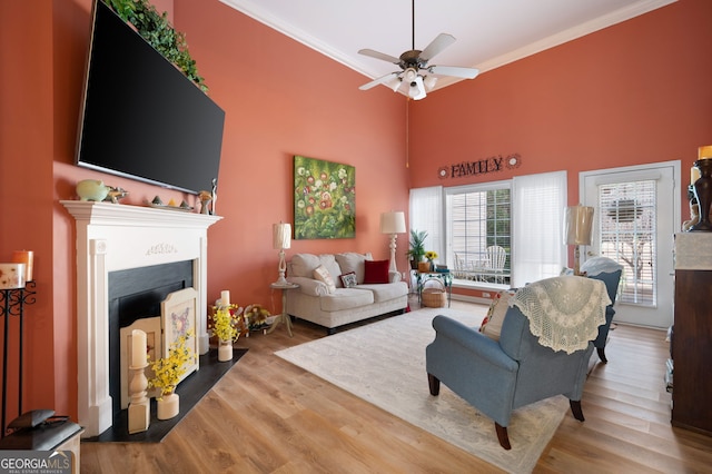 living room featuring ceiling fan, a fireplace with flush hearth, ornamental molding, a towering ceiling, and wood finished floors