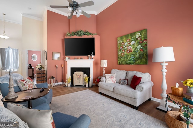 living room with ornamental molding, wood finished floors, baseboards, and ceiling fan