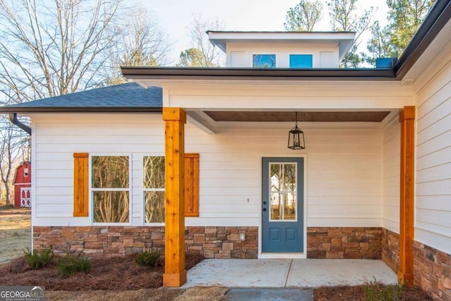 property entrance featuring stone siding, a porch, and roof with shingles