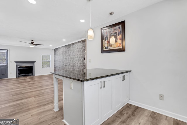 kitchen featuring a fireplace, hanging light fixtures, light wood-style floors, white cabinets, and a peninsula