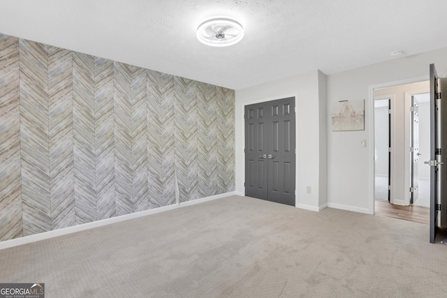 interior space featuring wallpapered walls, baseboards, an accent wall, carpet, and a textured ceiling