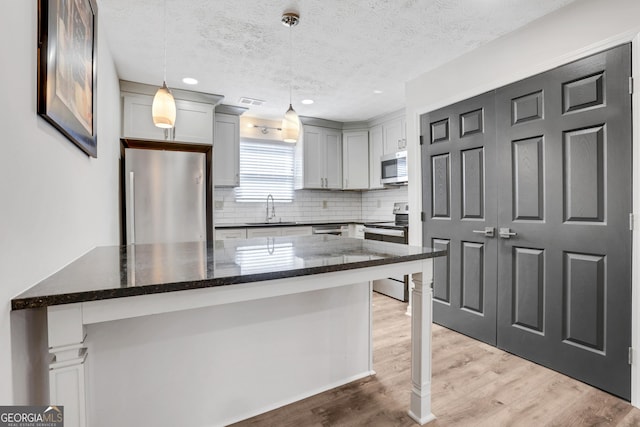 kitchen with tasteful backsplash, appliances with stainless steel finishes, dark stone countertops, wood finished floors, and a sink