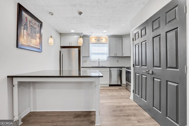 kitchen with stainless steel appliances, a sink, light wood finished floors, decorative light fixtures, and tasteful backsplash