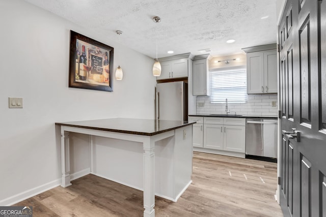 kitchen featuring dishwasher, dark countertops, light wood-style flooring, freestanding refrigerator, and a sink