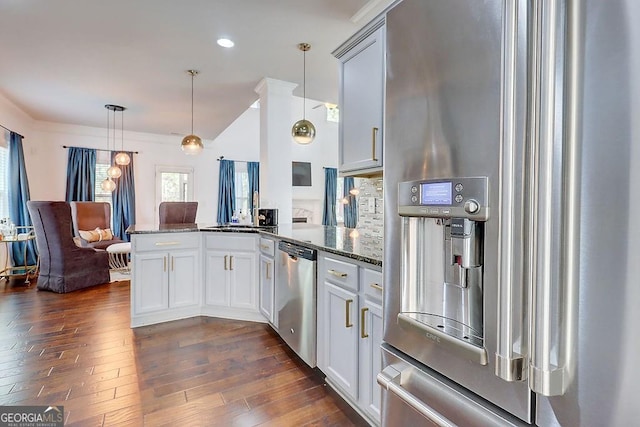 kitchen with a peninsula, dark wood-type flooring, hanging light fixtures, appliances with stainless steel finishes, and dark stone countertops