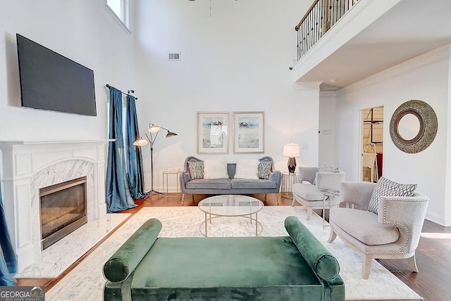 living area with a high ceiling, a fireplace, wood finished floors, visible vents, and baseboards