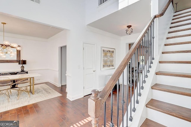 stairway with baseboards, a high ceiling, a chandelier, and wood finished floors