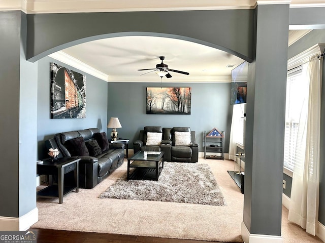 carpeted living area with ceiling fan, ornamental molding, arched walkways, and baseboards