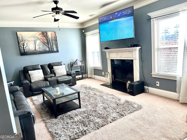 carpeted living room with ceiling fan, visible vents, baseboards, a high end fireplace, and crown molding