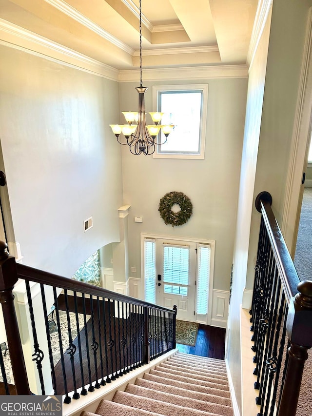 stairway featuring a notable chandelier, visible vents, ornamental molding, wainscoting, and a raised ceiling