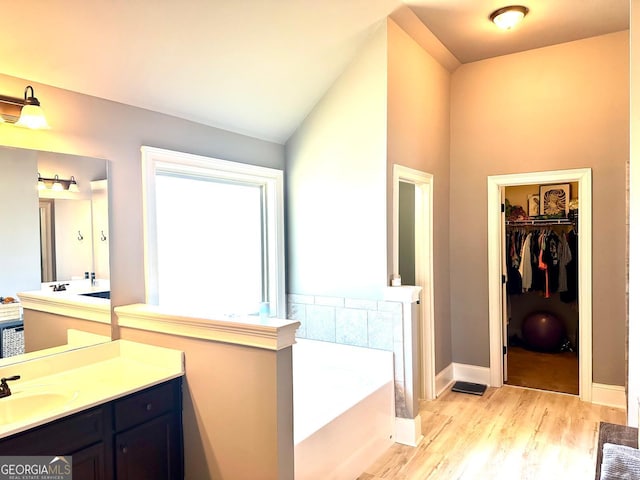 bathroom featuring wood finished floors, a walk in closet, vaulted ceiling, vanity, and a bath