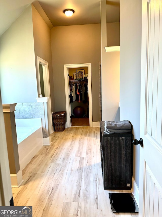 full bathroom with a walk in closet, vanity, wood finished floors, baseboards, and a bath