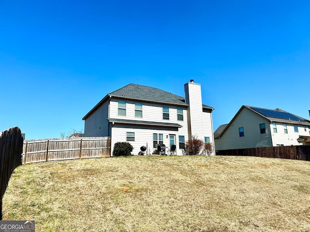 rear view of property featuring a fenced backyard, a yard, and a chimney